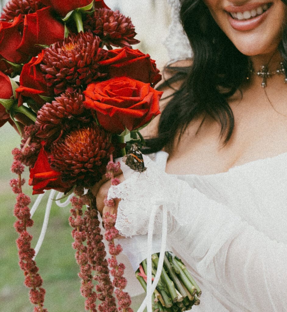 Detail photo of a butterfly on the bride's hand while she holds a bouquet 